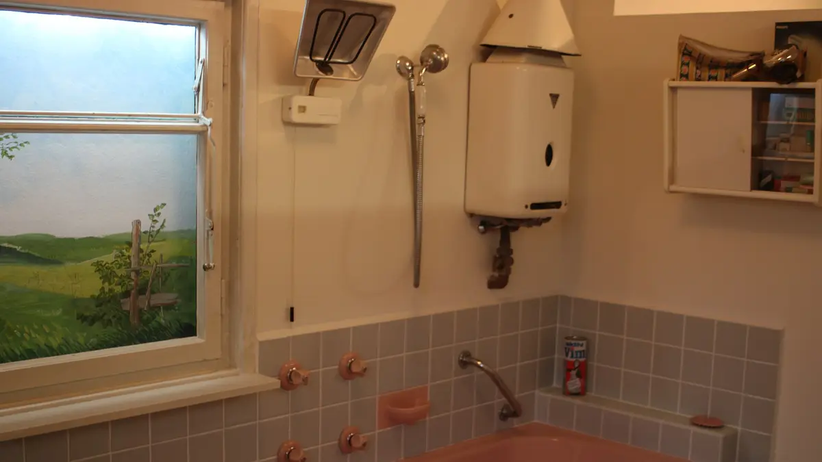 Baño de los años sesenta con un calentador de agua a gas sobre la tina