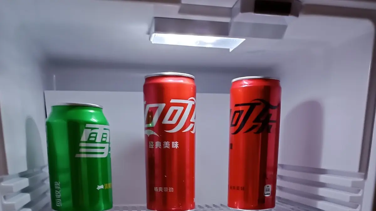 Interior iluminado de um frigobar com três latas de refrigerante em uma prateleira