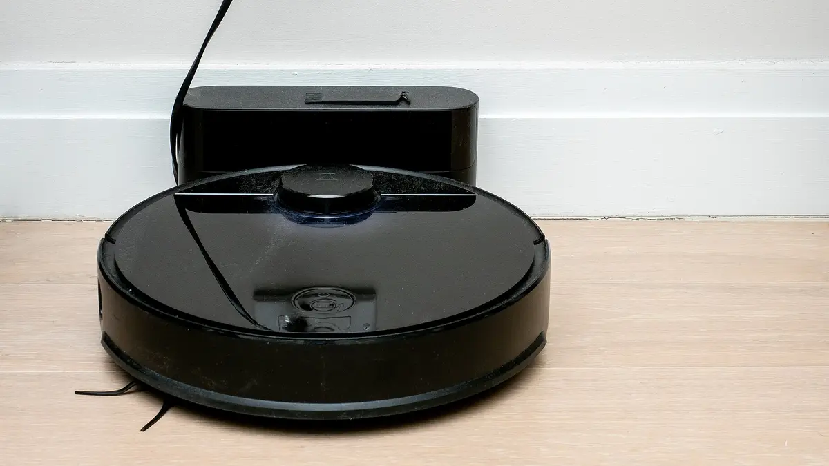 Aspirador robô preto conectado à base de carga junto à parede