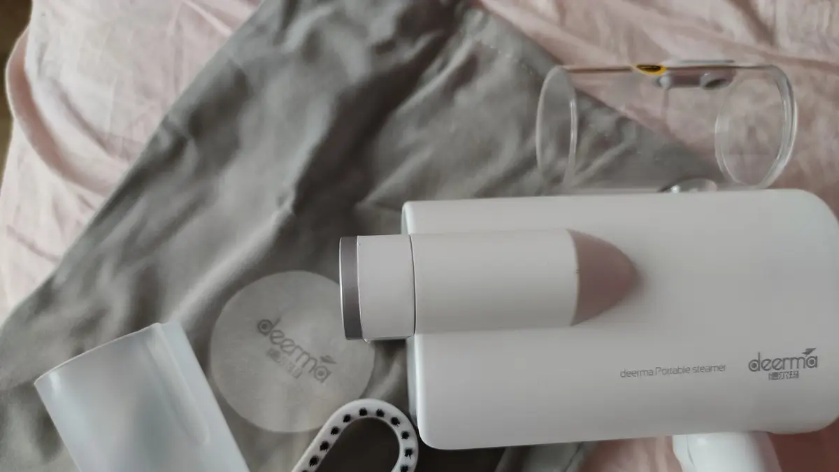 Vaporizador de ropa de mano blanco sobre una prenda, con sus accesorios